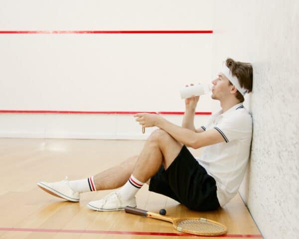 Tennisspieler, der auf dem Boden sitzt und Wasser aus einer Trinkflasche trinkt.